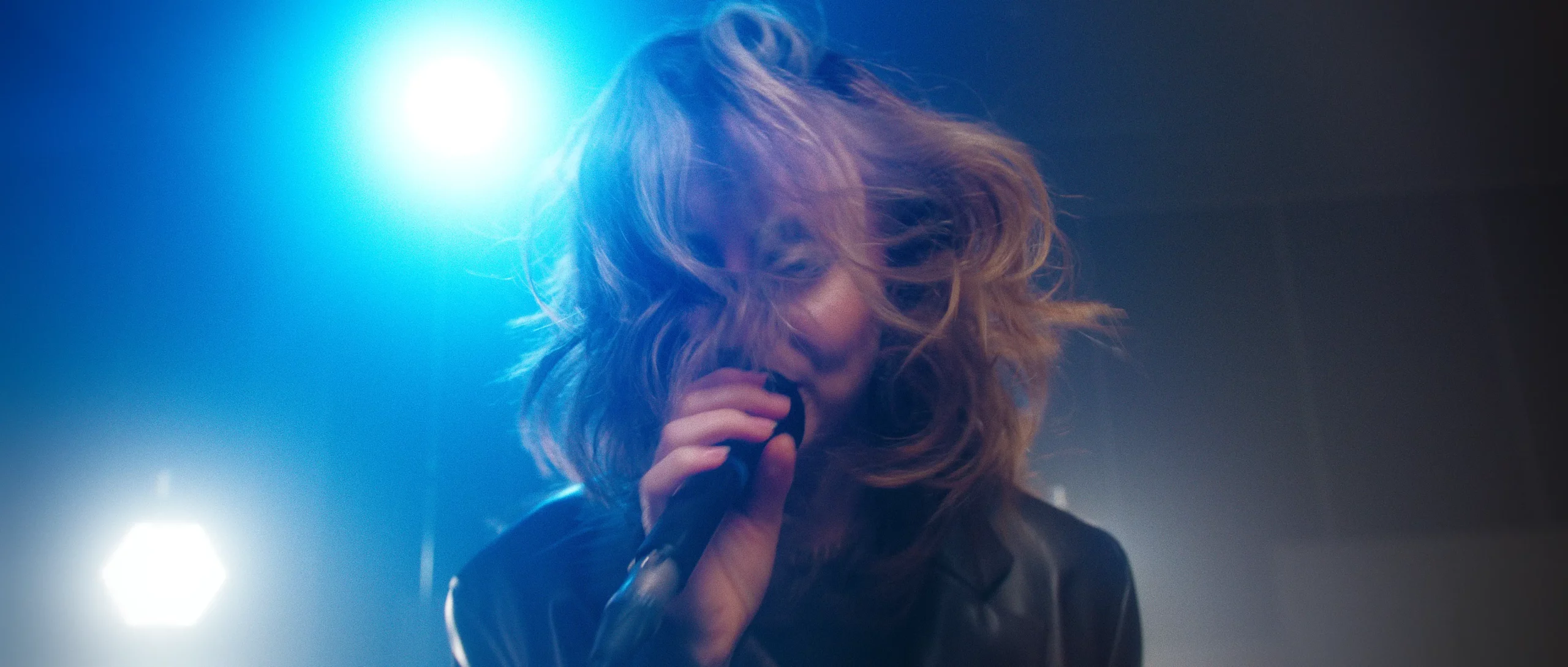 Singer with energetic hair, singing into microphone.